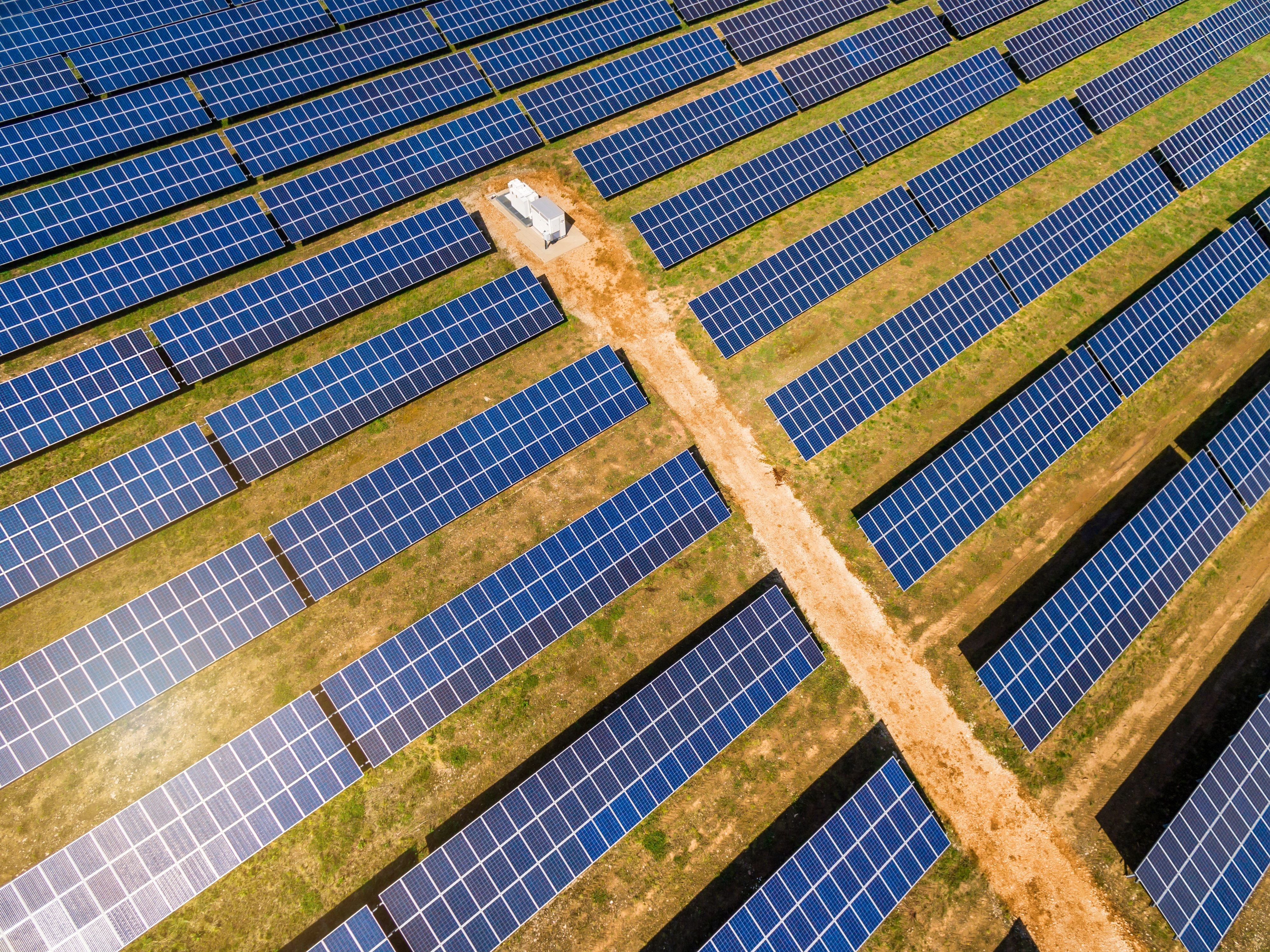 Aerial view of solar module rows crossed by a service track