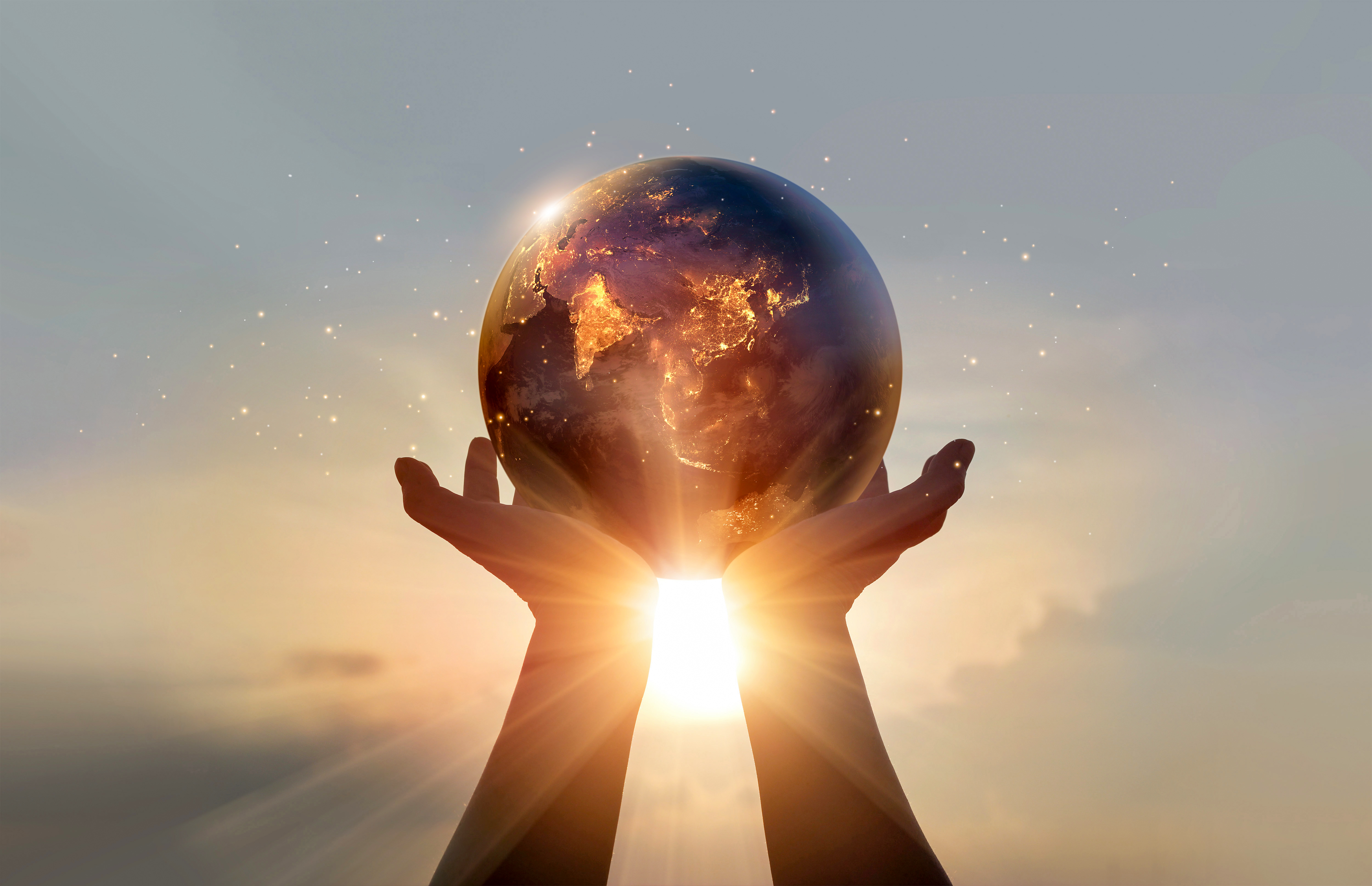 Hands holding a glowing globe against a sunrise
